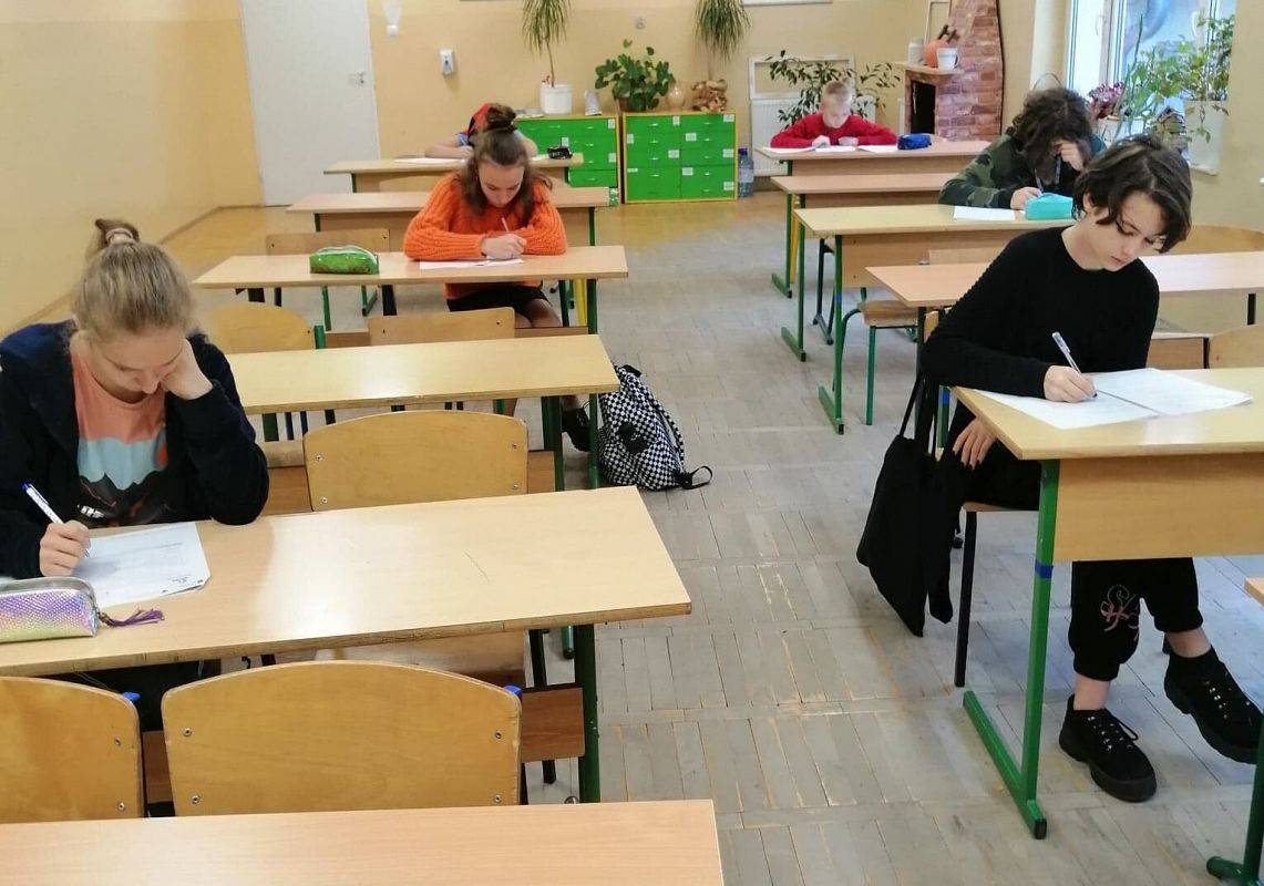 Uczniowie siedzą w szkolnych ławkach i rozwiązują test