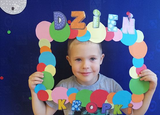 Przedszkolak  trzymający ramkę w kropki.