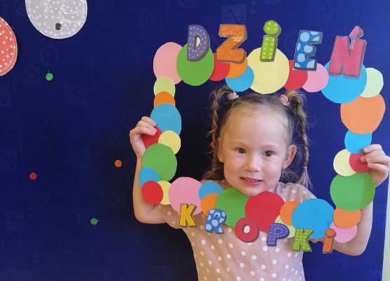 Przedszkolak  trzymający ramkę w kropki.