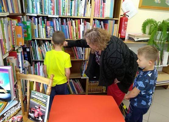 Uczniowie wraz z panią bibliotekarką przeglądają książki na półkach.