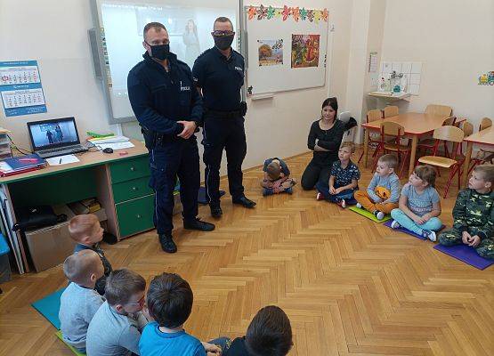 Dwaj policjanci opowiadają dzieciom o zagrożeniach na drogach.