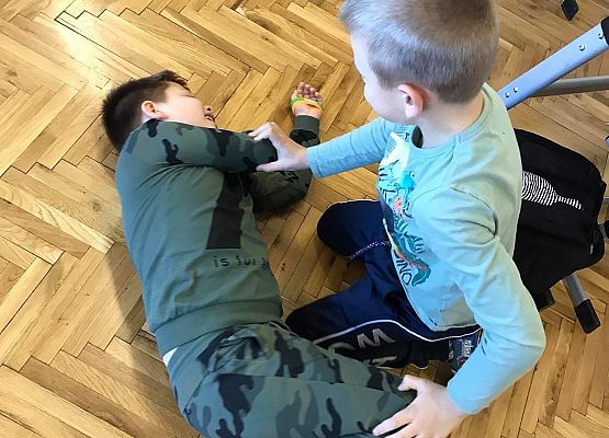 Dwaj chłopcy ćwiczą układanie w pozycję boczną bezpieczną.