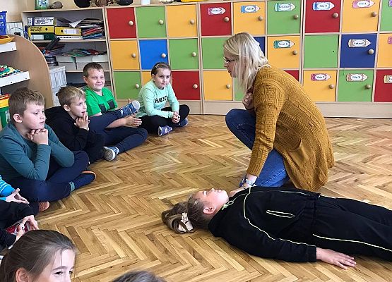 Pani instruuje dzieci zebrane w kółko w jaki sposób sprawdzamy czy poszkodowanemu coś się stało.