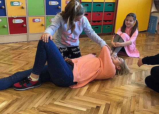 Pani leży na podłodze dzieci patrzą i się uczą. Dziewczynka układa panią w pozycji bocznej ustalonej.