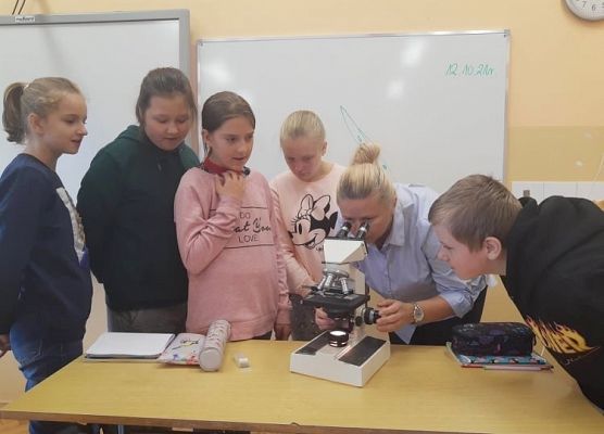 Nauczycielka pokazuje uczniom zasady korzystania z mikroskopu