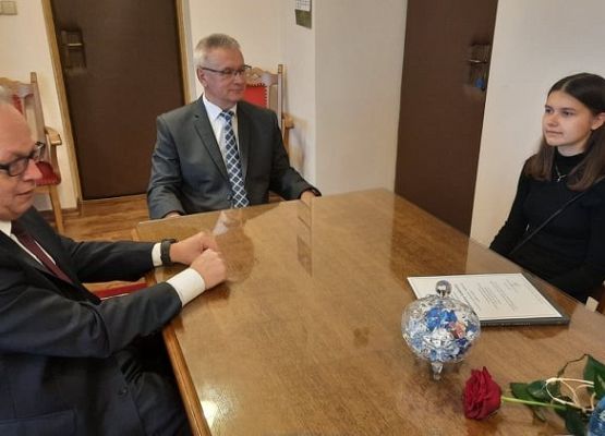 Przy stole siedzą: dyrektor szkoły, wójt i uczennica.