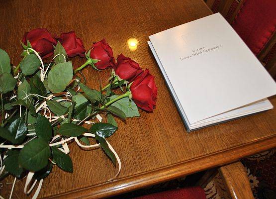 Na stole czerwone róże i teczka z napisem Gmina Nowa Wieś Lęborska