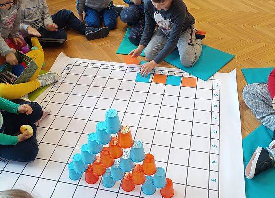 Dzieci odwzorowują wieżę z kubków na macie do kodowania za pomocą kolorowych kartoników