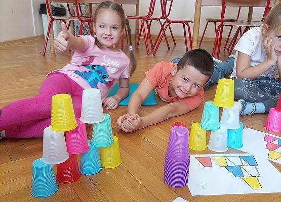 Dziewczynka i chłopiec ułożyli wieżę z kolorowych kubków zgodnie z podanym wzorem