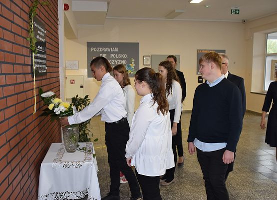 Delegacja uczniów składająca wiązankę przy tablicy patrona