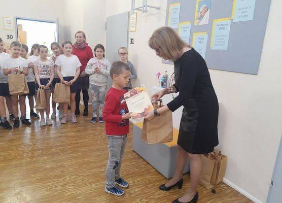 Uczeń odbiera dyplom i nagrodę od pani dyrektor.