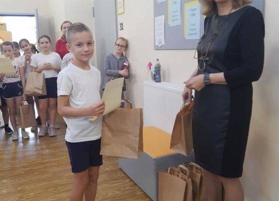 Uczeń odbiera dyplom i nagrodę od pani dyrektor.