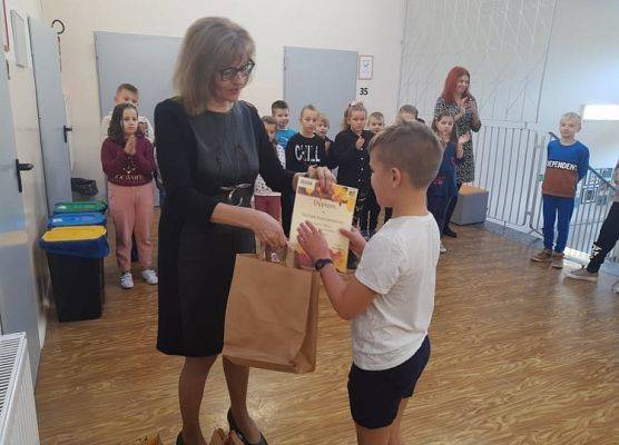 Uczeń odbiera dyplom i nagrodę od pani dyrektor.