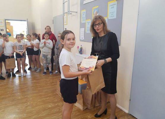 Uczennica odbiera dyplom i nagrodę od pani dyrektor.