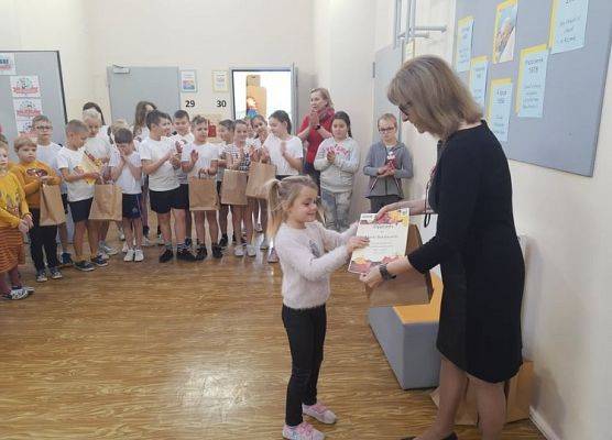 Uczennica odbiera dyplom i nagrodę od pani dyrektor.