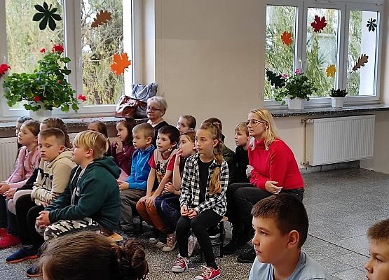 Uczniowie siedzą na ławkach i słuchają policjantów