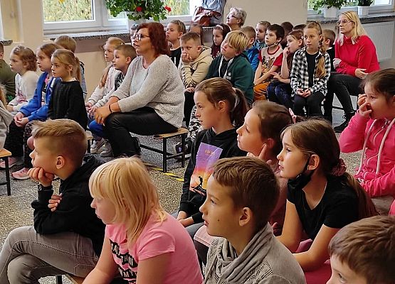 Uczniowie siedzą na ławkach i słuchają policjantów