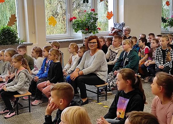 Uczniowie siedzą na ławkach i słuchają policjantów