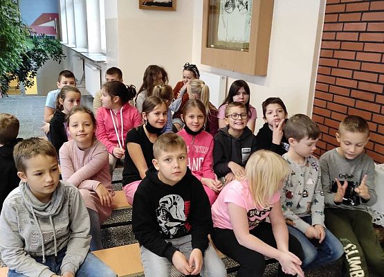 Uczniowie siedzą na ławkach i słuchają policjantów