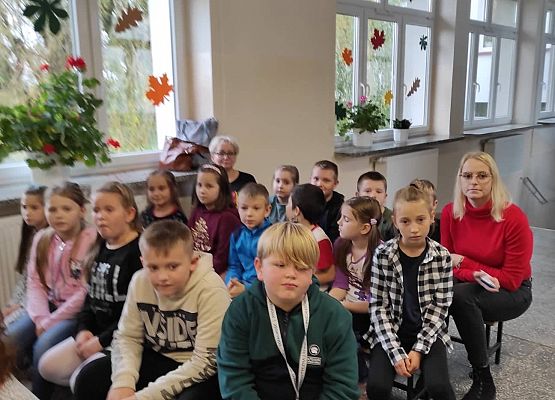 Uczniowie siedzą na ławkach i słuchają policjantów