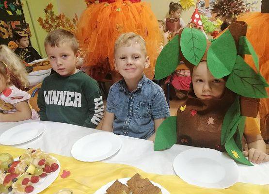 Dzieci w przebraniach siedzą przy stoliku podczas słodkiego poczęstunku