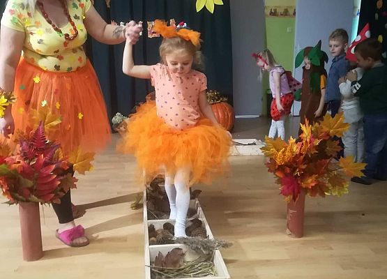 Dziewczynka  w asyście nauczycieli przechodzi przez ścieżkę sensoryczną