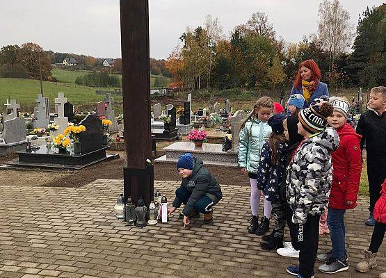 Uczniowie pod krzyżem na cmentarzu w Łebieniu ustawiają znicz z napisem Szkoła Pamięta