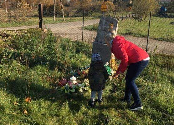 Przedszkolak w asyście nauczyciela ustawia znicz na nagrobku