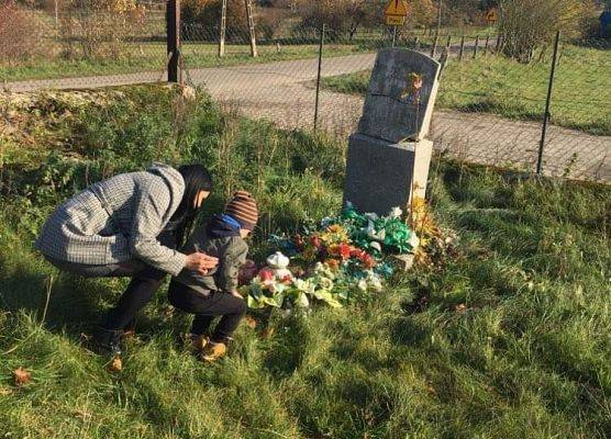 Przedszkolak w asyście nauczyciela ustawia znicz na nagrobku