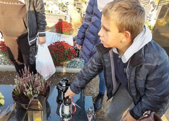 Uczeń stawia na nagrobku znicz z napisem Szkoła Pamięta