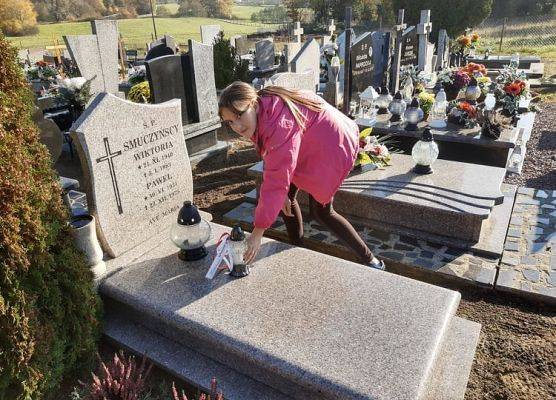 Uczennica stawia na nagrobku znicz z napisem Szkoła Pamięta