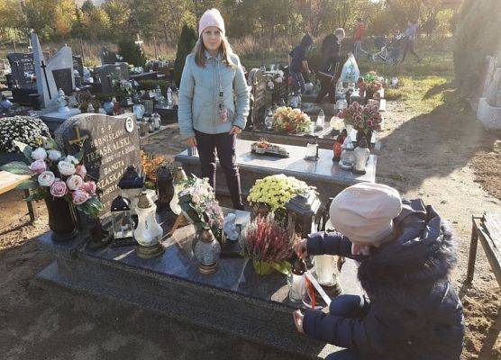 Uczennice stawiają na nagrobku znicz z napisem Szkoła Pamięta