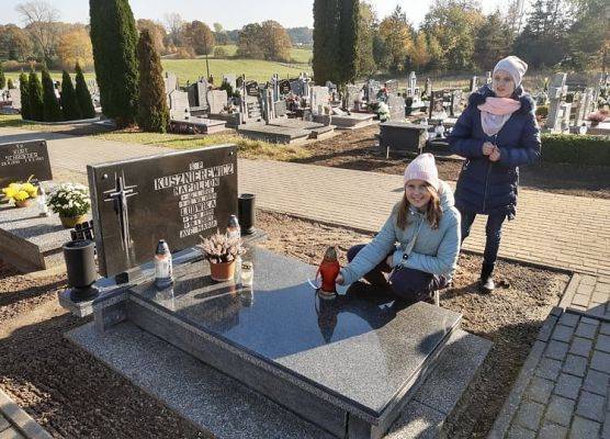 Uczennica stawia na nagrobku znicz z napisem Szkoła Pamięta