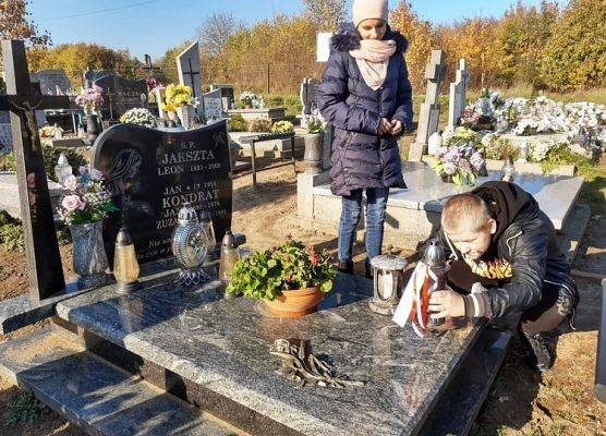 Uczeń stawia na nagrobku znicz z napisem Szkoła Pamięta