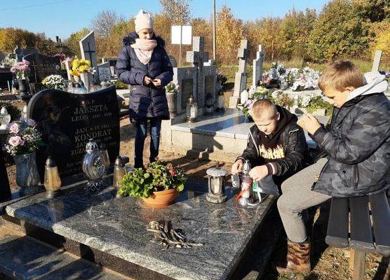 Uczeń stawia na nagrobku znicz z napisem Szkoła Pamięta