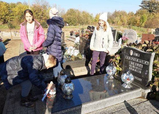 Uczeń stawia na nagrobku znicz z napisem Szkoła Pamięta