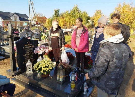 Uczniowie stoją na cmentarzu przy nagrobku