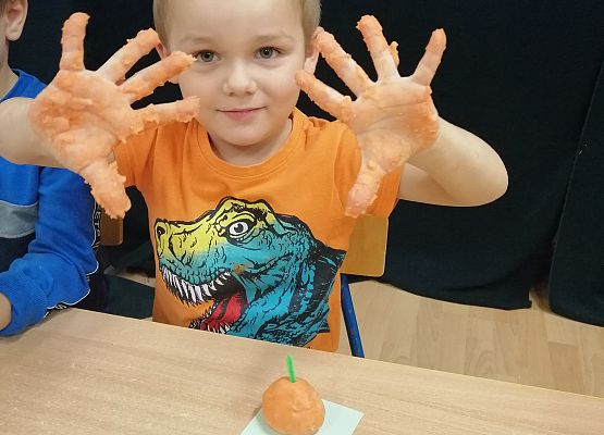 Chłopiec prezentuje wykonaną przez siebie dynię oraz ubrudzone rączki