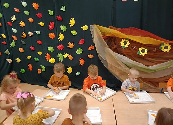 Dzieci siedzą przy stoliku i wykonują prace plastyczne