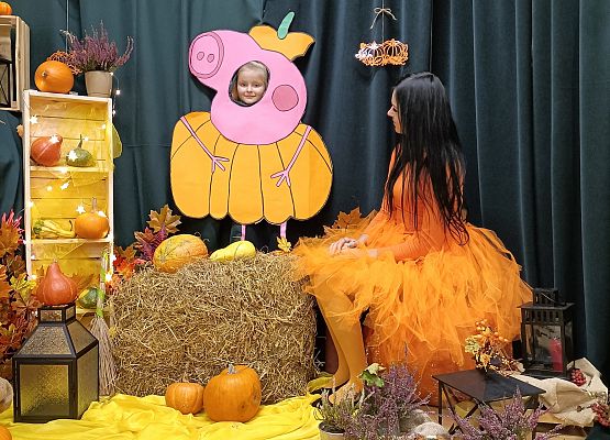 Dziecko pozuje do zdjęcia w makiecie dyni obok siedzi