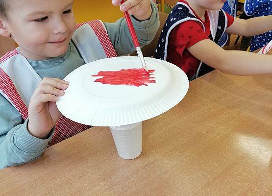 Chłopiec maluje papierowy talerzyk czerwoną farbą