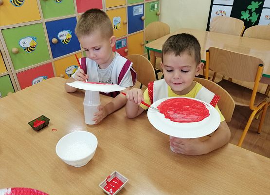 Chłopcy malują papierowe talerzyki czerwoną farbą