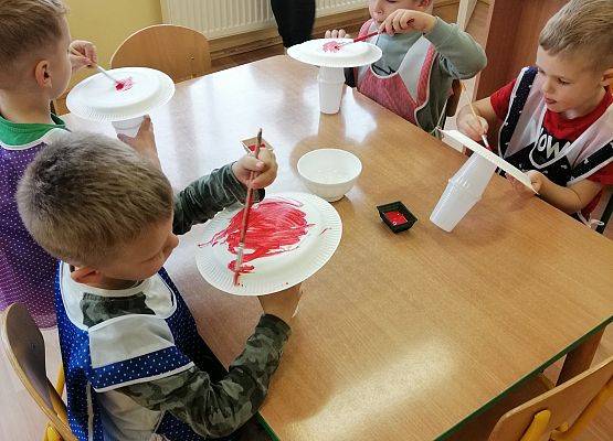Chłopcy malują papierowe talerzyki czerwoną farbą