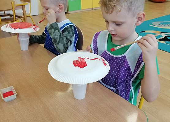 Chłopcy malują papierowe talerzyki czerwoną farbą