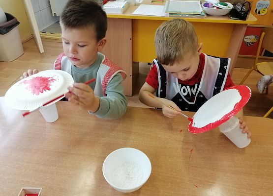 Chłopcy malują papierowe talerzyki czerwoną farbą