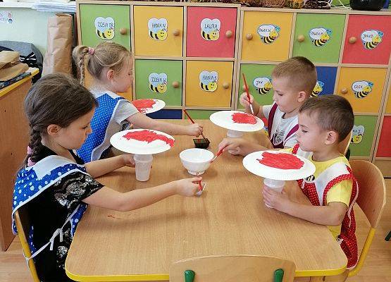 Dzieci malują papierowe talerzyki czerwoną farbą