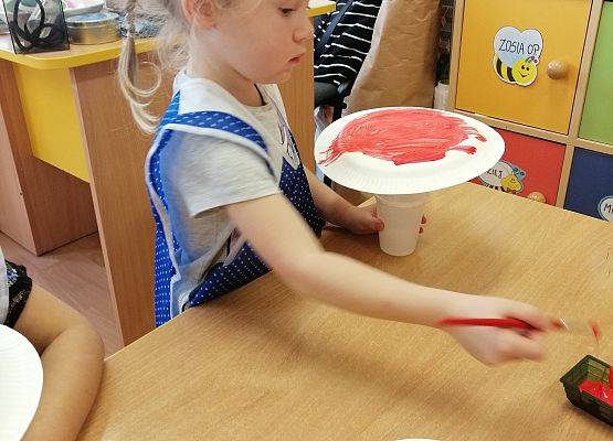 Dziewczynka maluje papierowy talerz czerwoną farbą