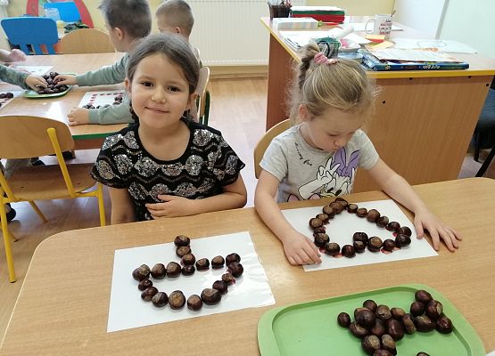 Dziewczynki układają różne kształty z kasztanów