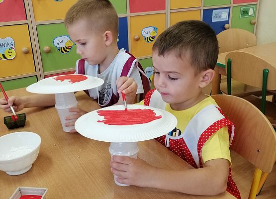 Chłopcy malują papierowe talerzyki czerwoną farbą