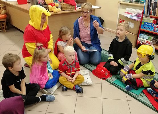 Dzieci siedzą w bibliotece i słuchają bajki